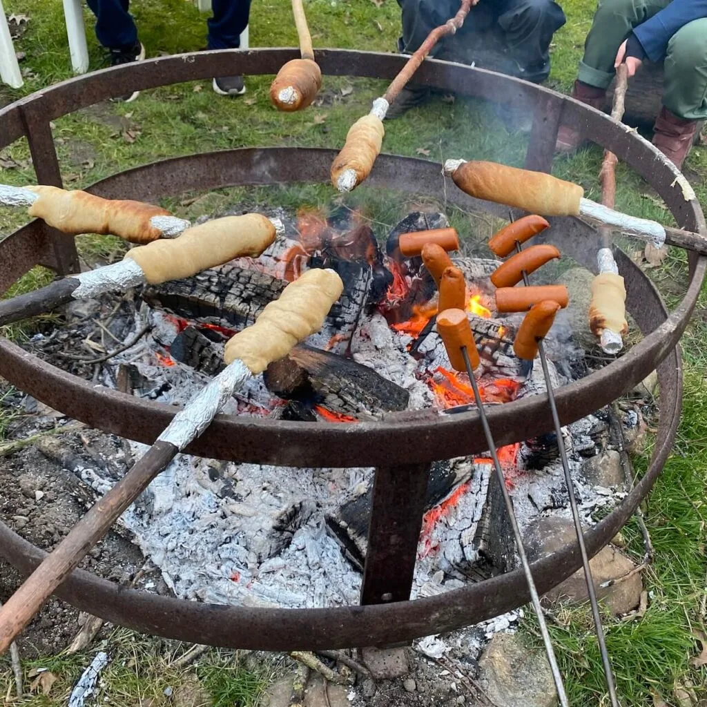 Stockbrot und Würstchen werden über einer Feuerstelle zubereitet, Teil des Hoflebens auf Hof Schlünzen in Ostholstein